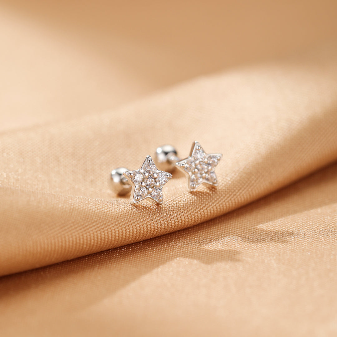 Paire de boucles d'oreilles étoiles en argent 925 ornées de zircons brillants, sur fond satiné doré.
