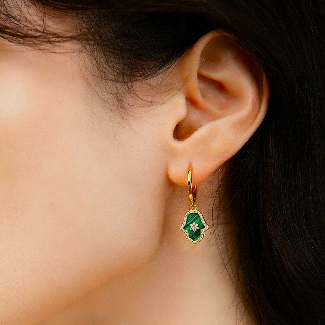 Boucle d'oreille plaqué or avec une main de Fatma en malachite sertie d'une étoile et de petites pierres blanches sur l'oreille d'une femme.