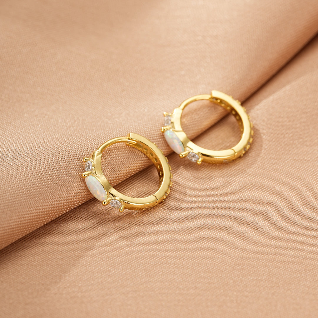 Boucles d'oreilles créoles dorées ornées d'opales et de zirconiums, sur fond de soie beige