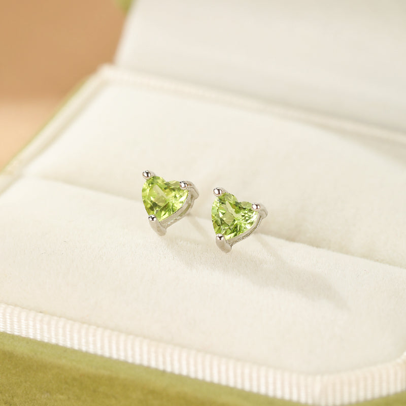 Paire de boucles d'oreilles en argent serties de péridots taillés en forme de cœur vert vif, présentées dans un écrin vert.