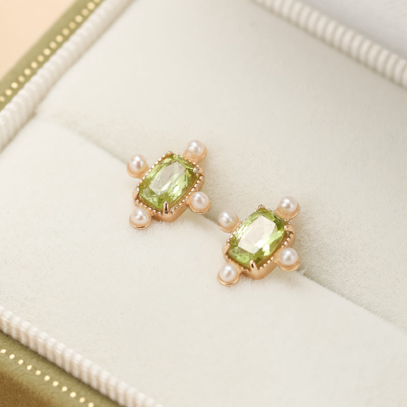 Paire de boucles d'oreilles en argent plaqué or serties d'une pierre péridot rectangulaire entourée de petites perles blanches, dans un écrin.