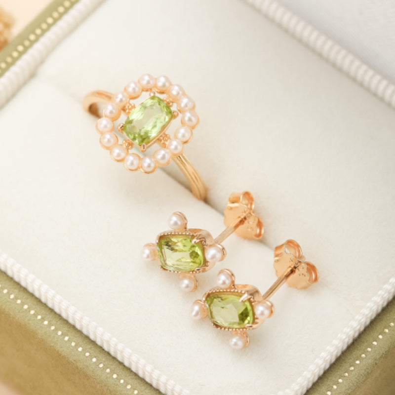 Boucles d'oreilles carrées plaquées or avec péridot et perles, présentées avec une bague assortie dans une boîte à bijoux.