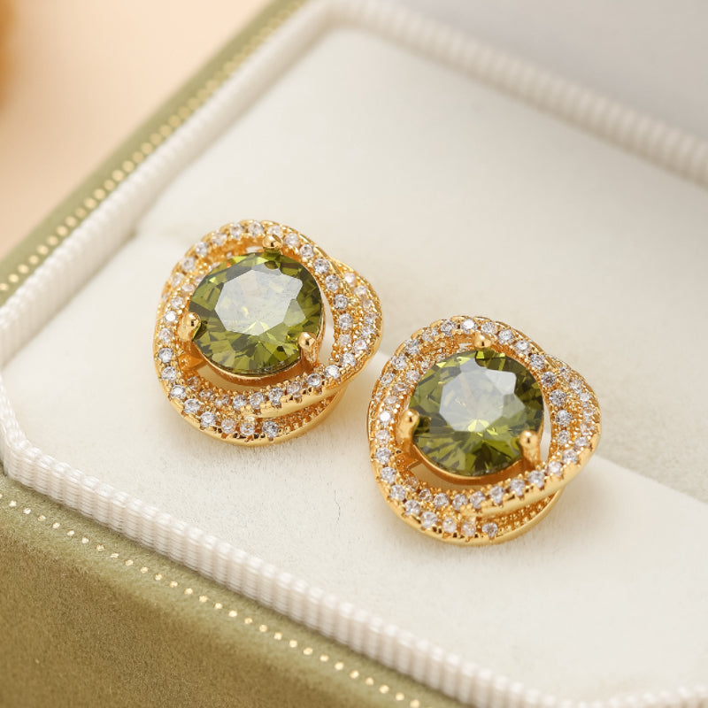Paire de boucles d'oreilles en or avec une pierre centrale verte ronde et un entourage de petites pierres brillantes, dans un écrin.
