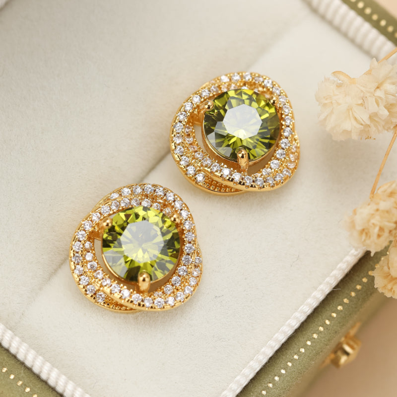 Paire de boucles d'oreilles en or ornées de péridots verts ronds et de petites pierres blanches scintillantes, présentées dans une boîte écrue.
