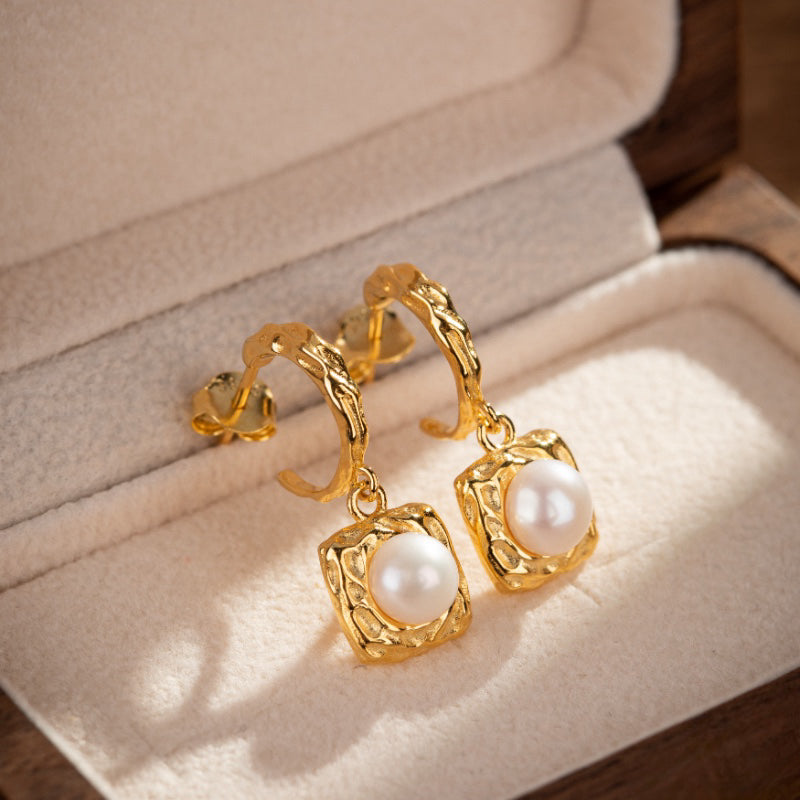 Boucles d'oreilles pendantes en argent plaqué or ornées d'une perle blanche, présentées dans leur écrin.