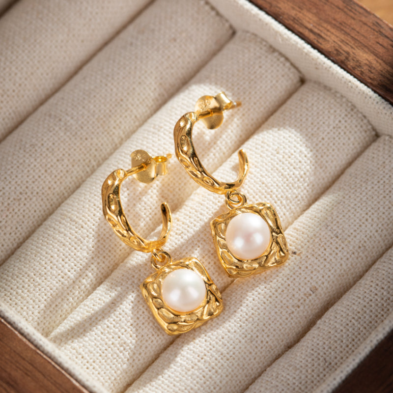 Boucles d'oreilles plaquées or avec une perle blanche centrale et un design carré texturé.