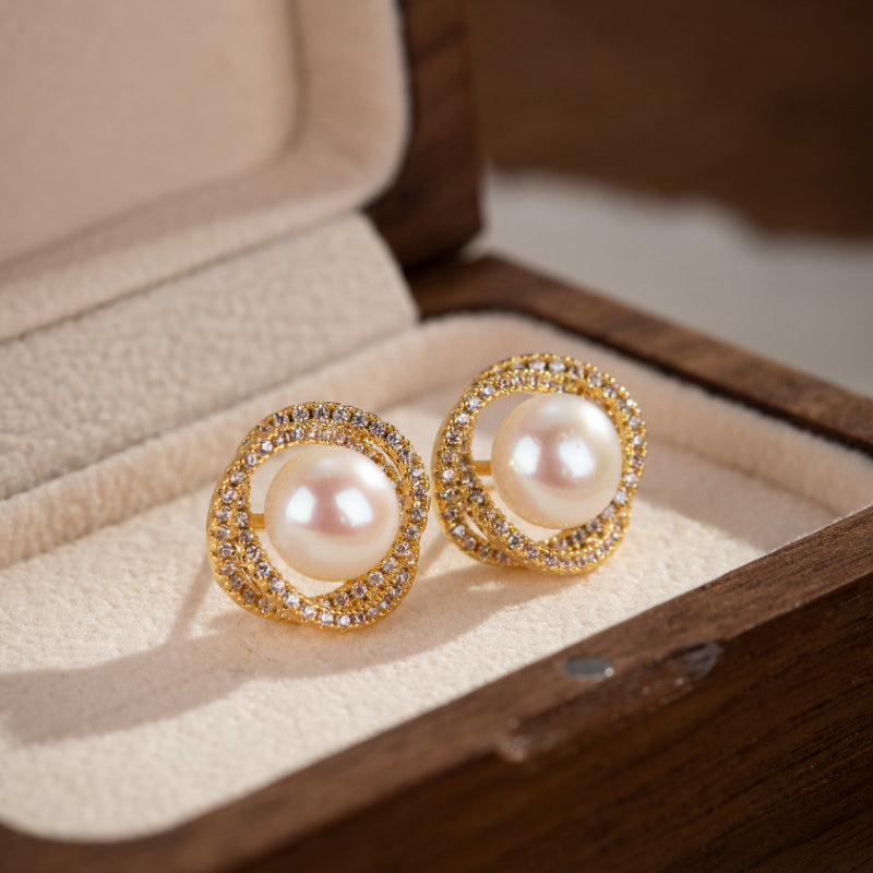 Paire de boucles d'oreilles en argent plaqué or ornées d'une perle centrale et d'une bordure de petites pierres scintillantes, présentées dans un écrin en bois.