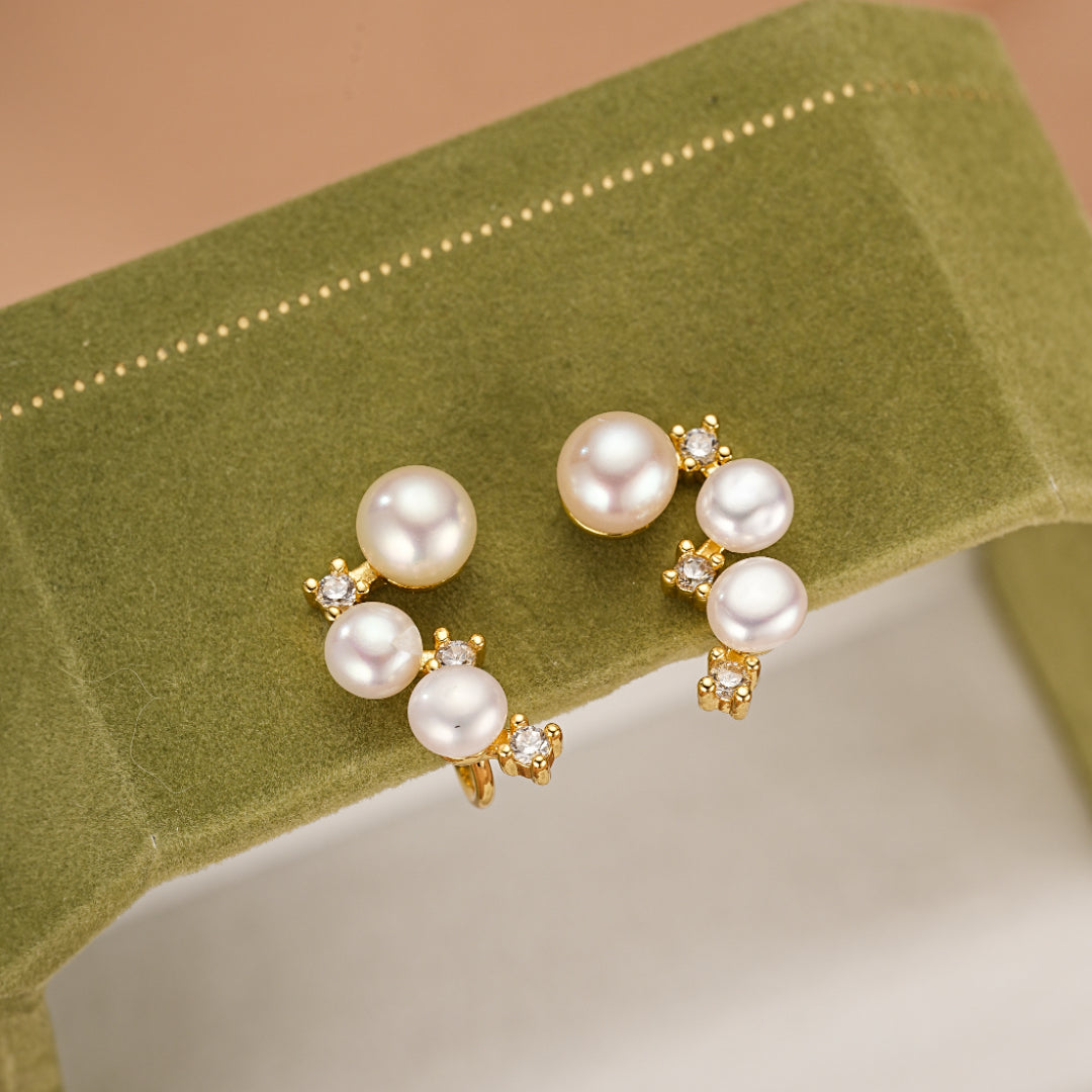 Paire de boucles d'oreilles plaqué or ornées de perles nacrées et de petits cristaux scintillants, disposées en cascade sur un écrin vert.