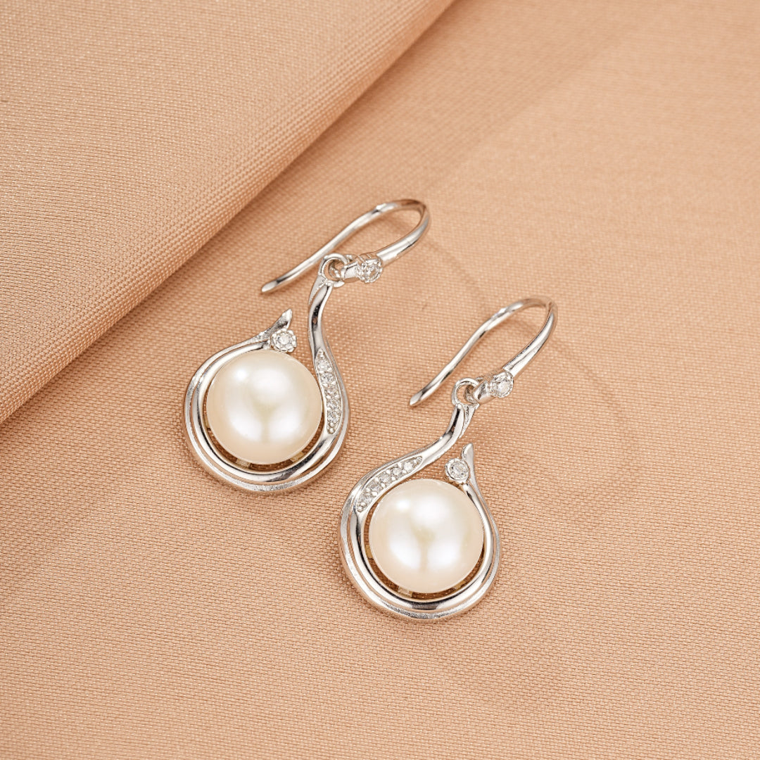 Boucles d'oreilles en argent ornées d'une perle blanche et de petits cristaux, en forme de goutte stylisée.