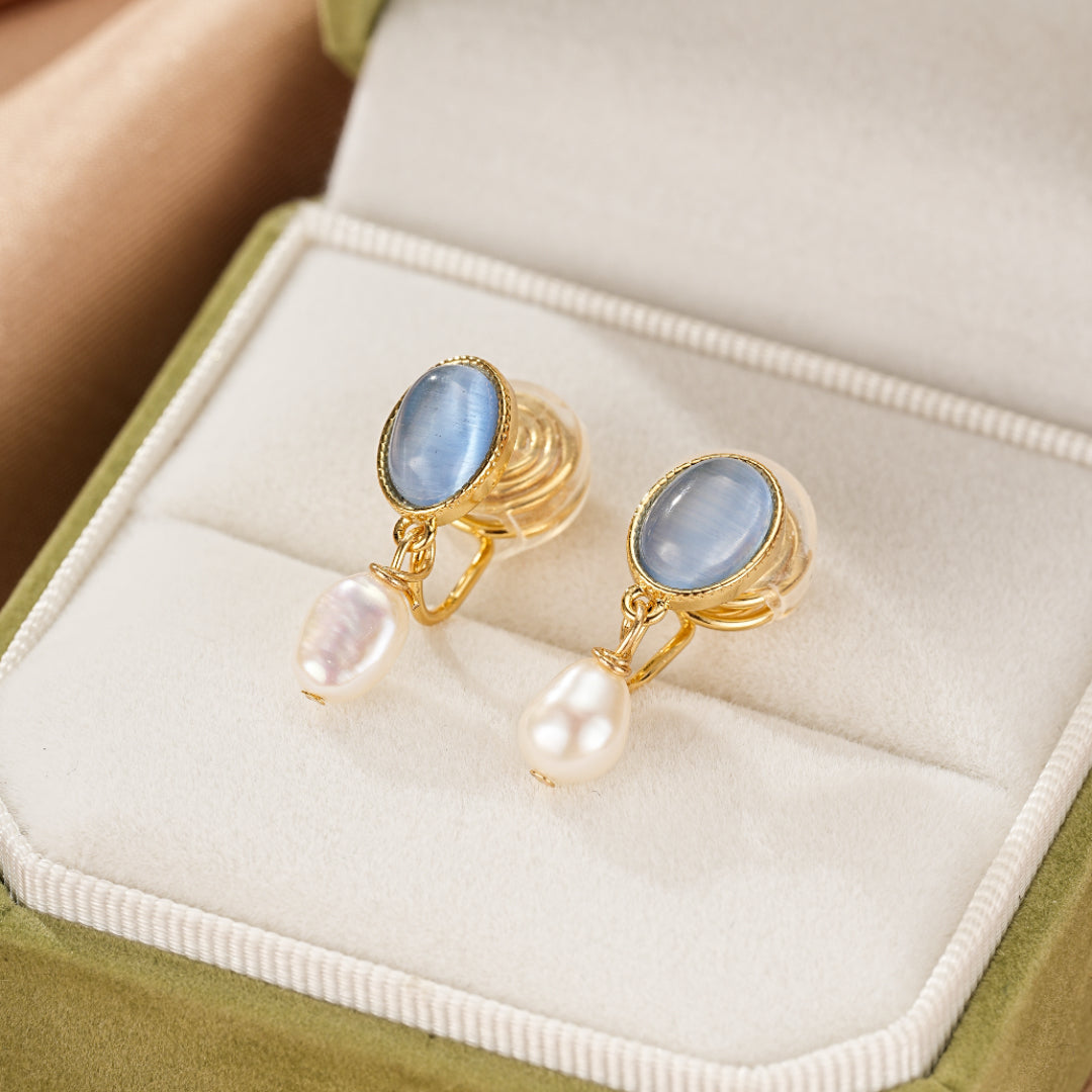 Boucles d’oreilles pendantes en or avec des pierres bleues ovales et des perles d’eau douce naturelles, présentées dans une boîte cadeau verte.