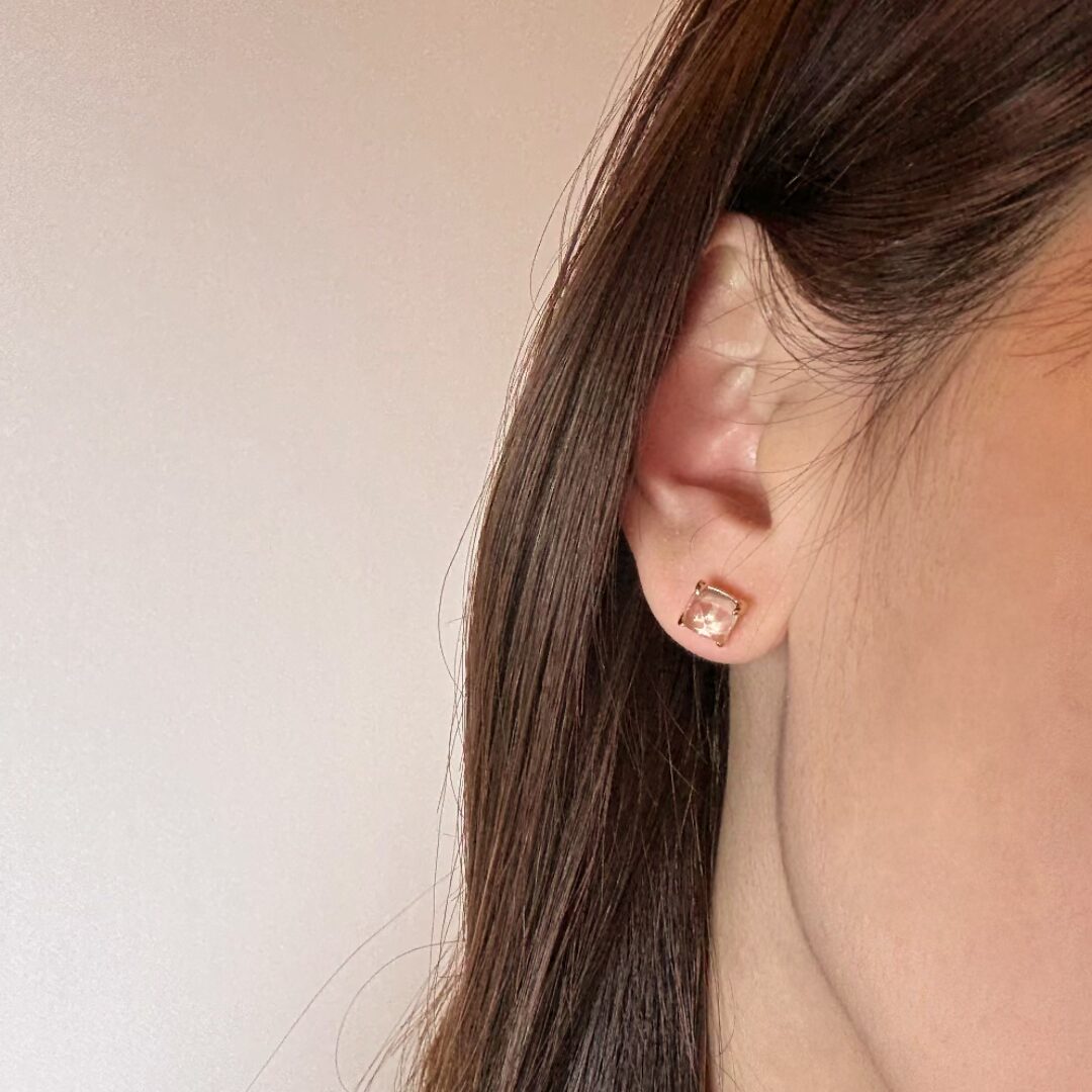 Boucle d'oreille carrée en quartz rose clair avec monture plaquée or, portée sur un lobe d'oreille.