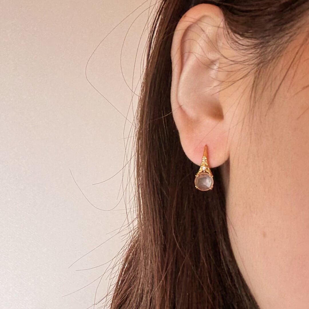 Boucle d'oreille en argent plaqué or ornée d'une pierre de quartz rose aux reflets délicats et de petits points lumineux sur le dessus.