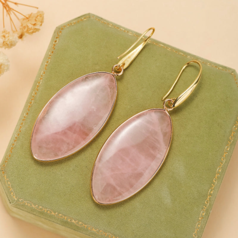 Boucles d'oreilles pendantes avec des pierres de quartz rose ovales montées sur un cadre doré fin et des crochets dorés.