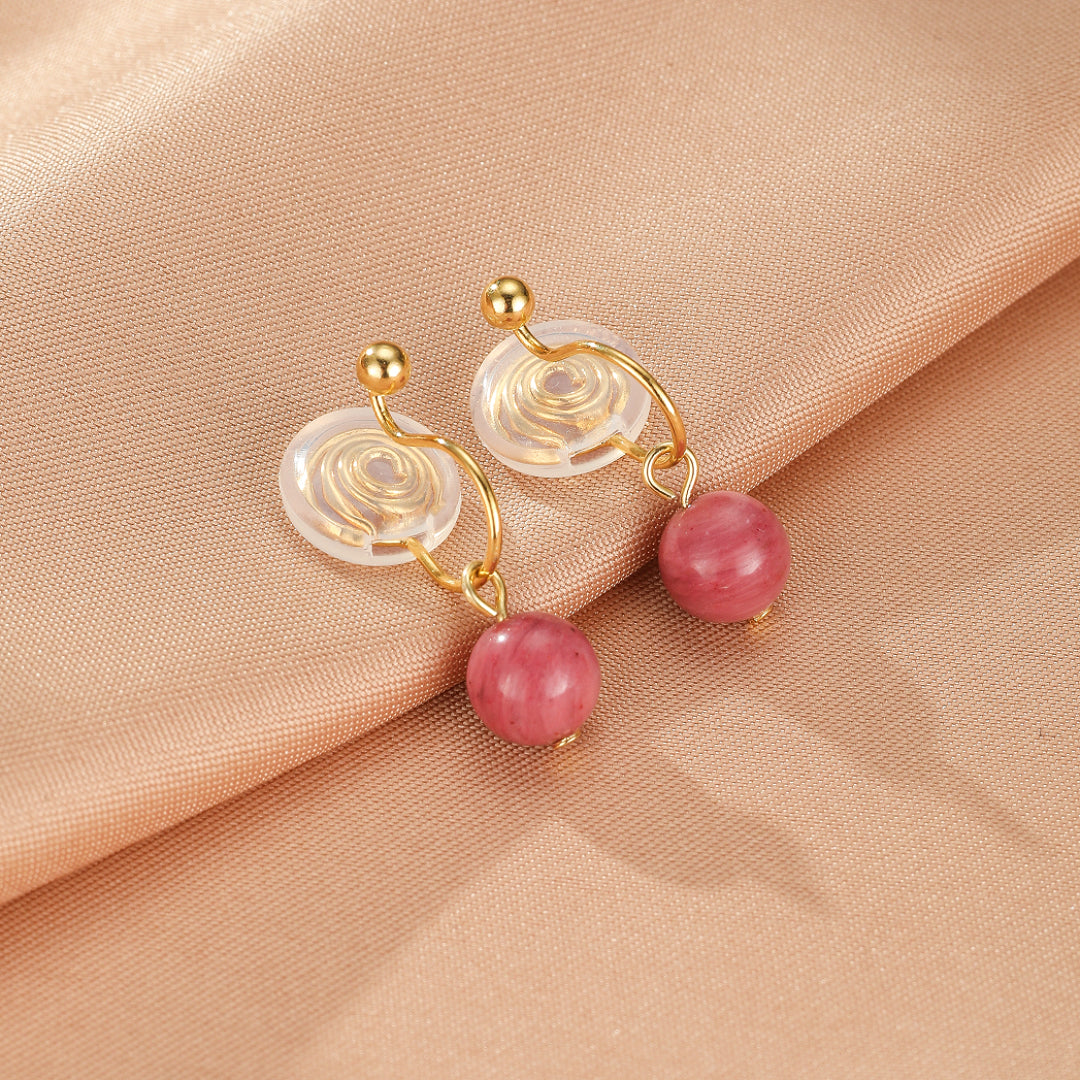 Paire de boucles d'oreilles pendantes en or avec des perles rondes en rhodonite rose, montées sur des supports transparents en spirale.
