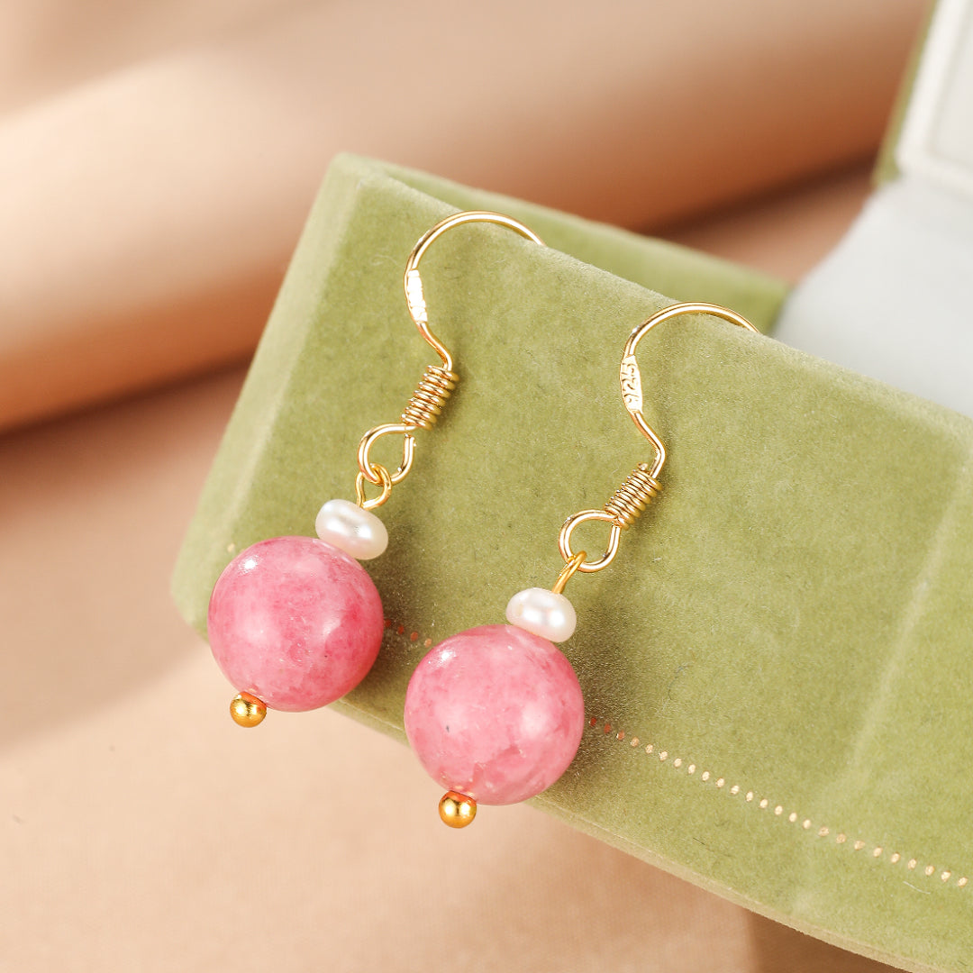 Boucles d'oreilles pendantes en argent plaqué or avec une perle rose de rhodonite ronde et une petite perle blanche sur un fermoir crochet.