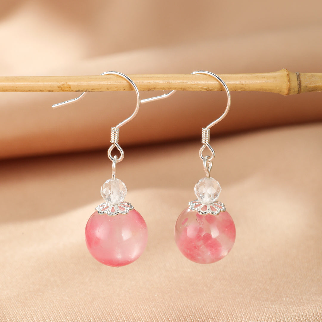 Boucles d’oreilles pendantes en argent avec une perle ronde rose en rhodonite et une petite perle de cristal transparente au-dessus.