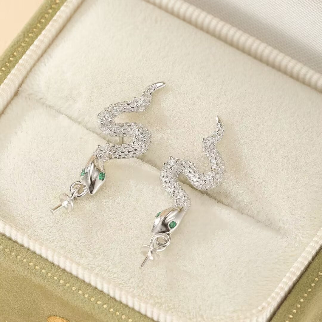 Paire de boucles d'oreilles serpent en argent 925 avec des yeux verts, posées dans un écrin.