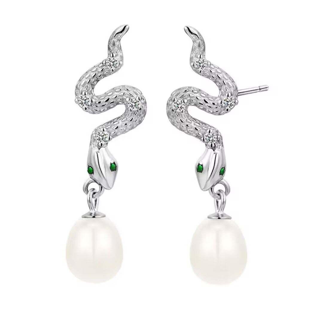 Paire de boucles d'oreilles en argent 925 en forme de serpent stylisé avec des yeux en émeraude et une perle blanche suspendue.