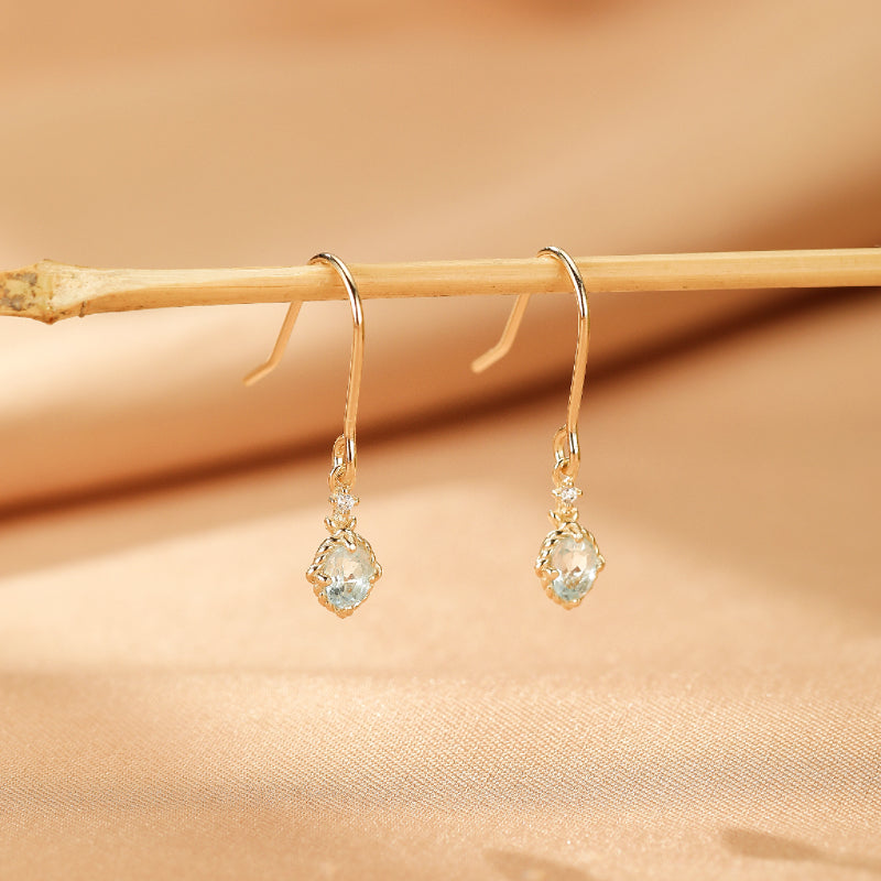Boucles d'oreilles pendantes plaquées or "Éclat d'Elysée" avec une topaze bleu clair et de petits cristaux scintillants.