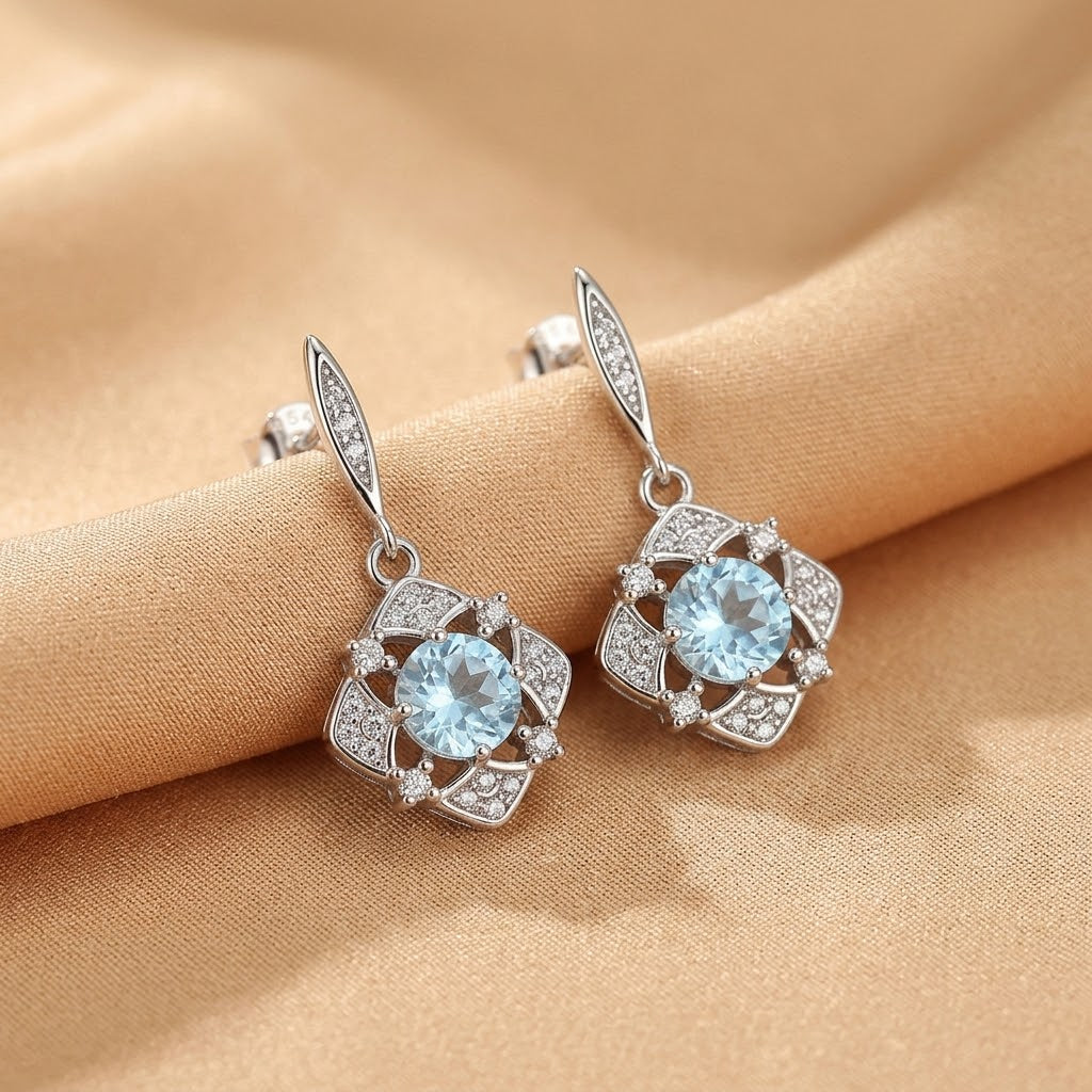 Boucles d'oreilles "Lumière d’Aurore" en argent serties de topazes bleues et de diamants scintillants, montées sur un fond satiné doré.