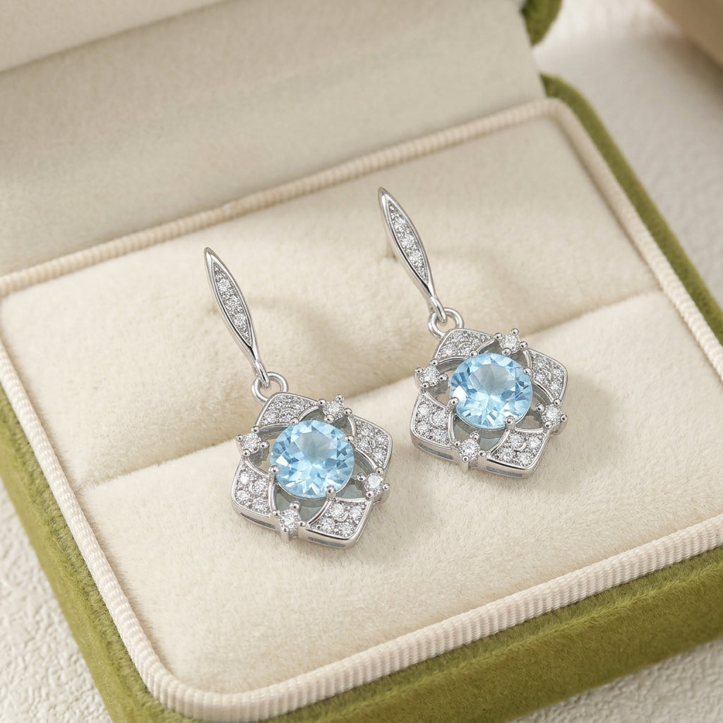 Boucles d'oreilles pendantes en argent ornées de topazes bleues et d'oxydes de zirconium, dans un écrin vert.