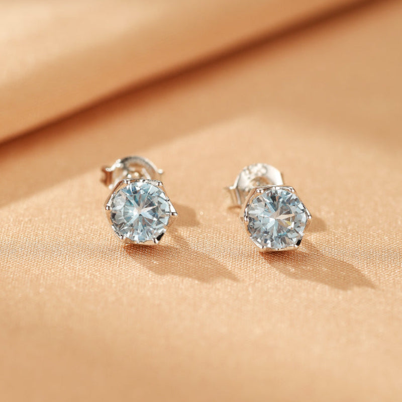 Boucles d'oreilles Topaze Argent Souffle Cristallin avec pierres bleues claires hexagonales sur un fond satiné doré.