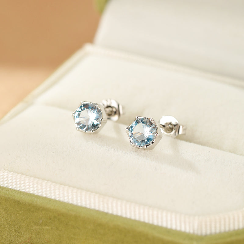 Boucles d'oreilles en argent avec une topaze bleue hexagonale sertie dans un écrin vert.