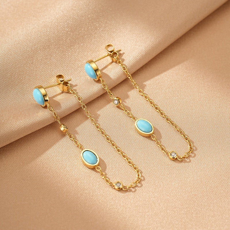 Boucles d'oreilles plaquées or avec des pierres turquoise ovales et des petites pierres scintillantes reliées par une fine chaîne.
