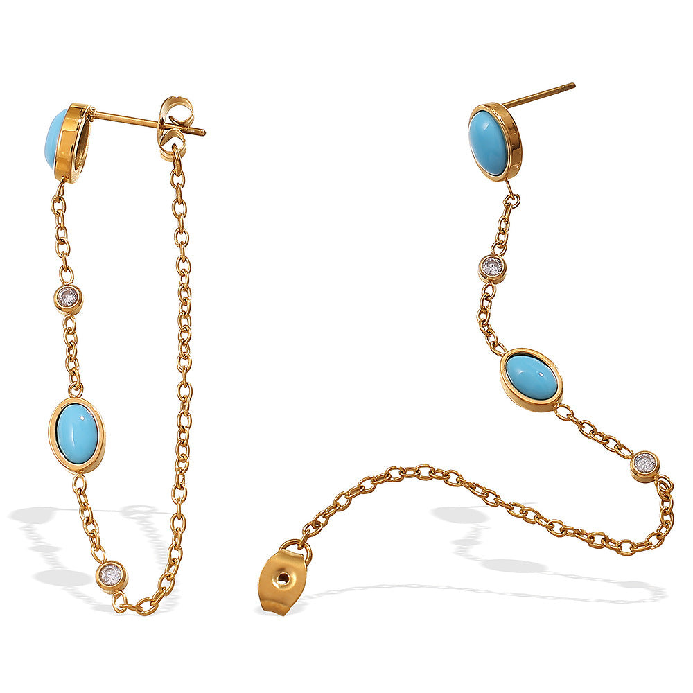 Boucles d'oreilles dorées avec une turquoise ovale et des cristaux incrustés, reliées par une fine chaîne.