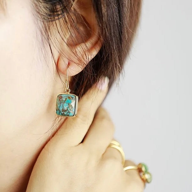 Boucles d'oreilles pendantes carrées en turquoise et argent plaqué or, ornées de détails bleus et verts, portées à l'oreille.