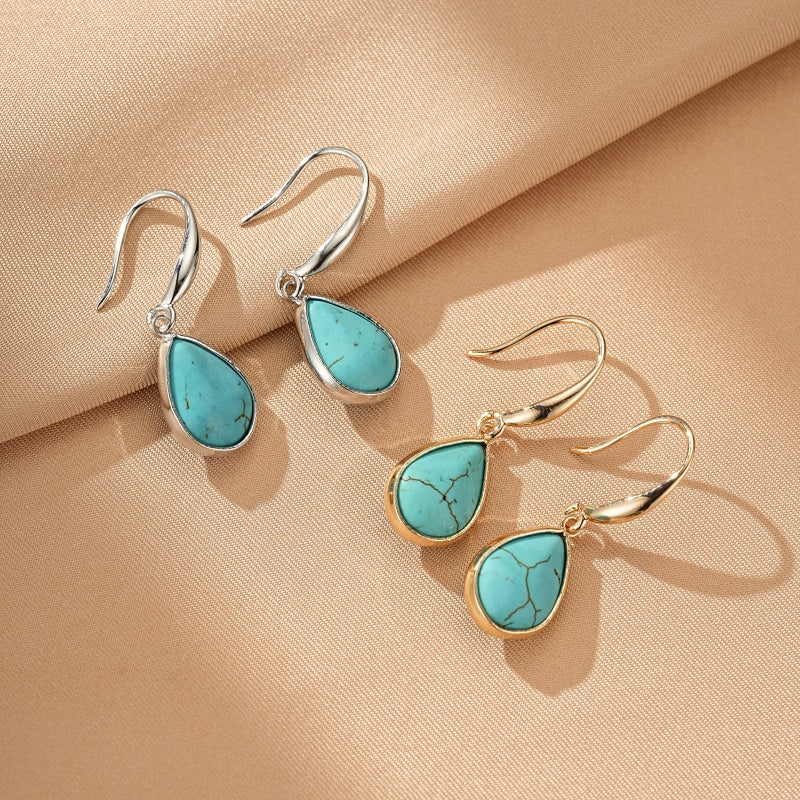 Boucles d'oreilles turquoise en forme de goutte, une paire argentée et une paire dorée, sur fond beige.