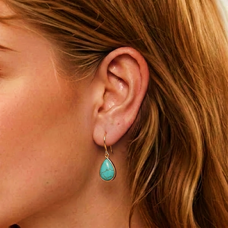 Goutte d'oreille turquoise sereine avec monture dorée suspendue à l'oreille d'une femme aux cheveux blonds.