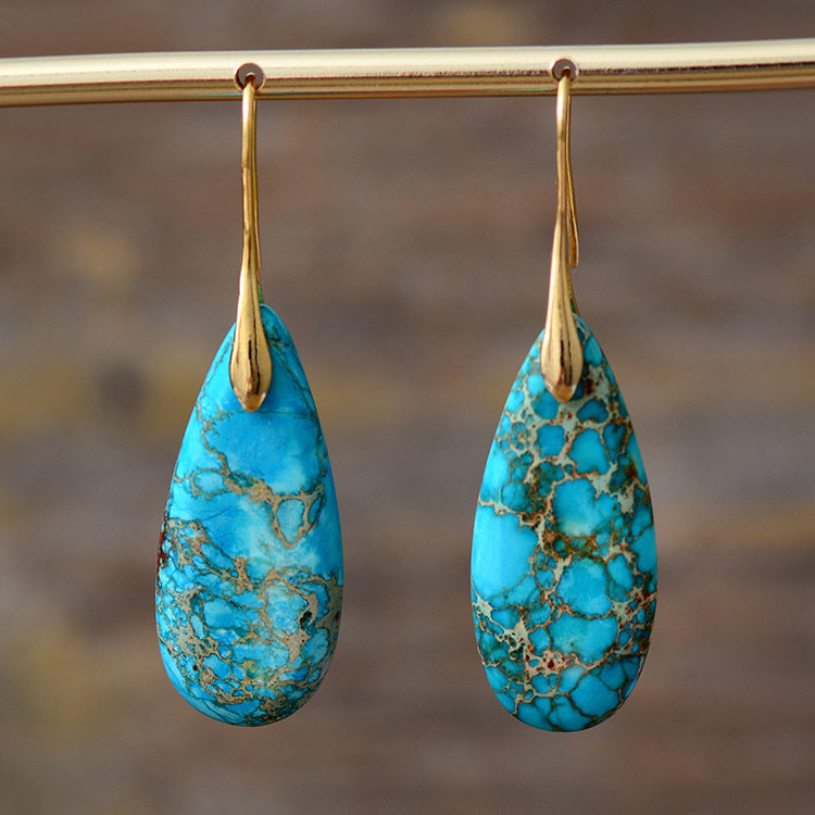Boucles d'oreilles majestueuses en turquoise et or avec des pierres bleues vives marbrées de motifs dorés.