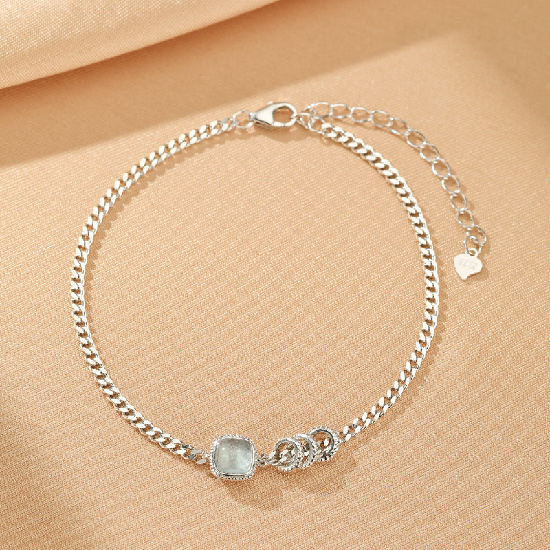 Bracelet en argent 925 avec une pierre carrée d'aigue-marine bleutée et trois anneaux entrelacés sur une chaîne gourmette.