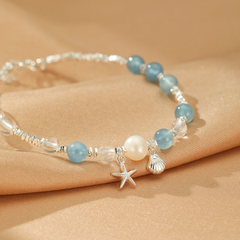 Bracelet fin en argent avec des perles d'aigue-marine bleues, une perle blanche nacrée, une étoile de mer et un coquillage.