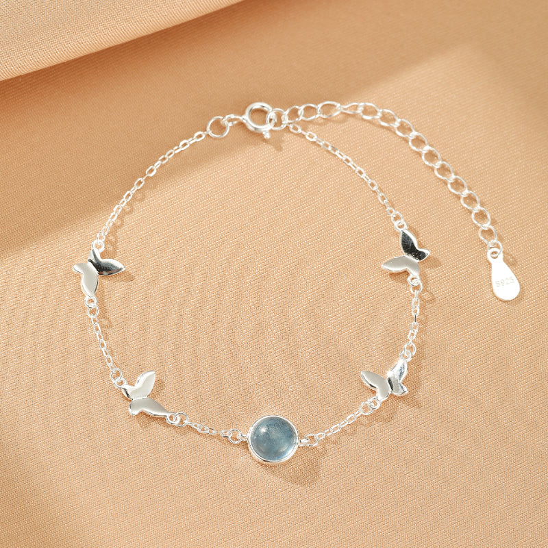 Bracelet en argent 925 avec une chaîne fine ornée de papillons argentés et d'une pierre bleue d'aigue-marine centrale.