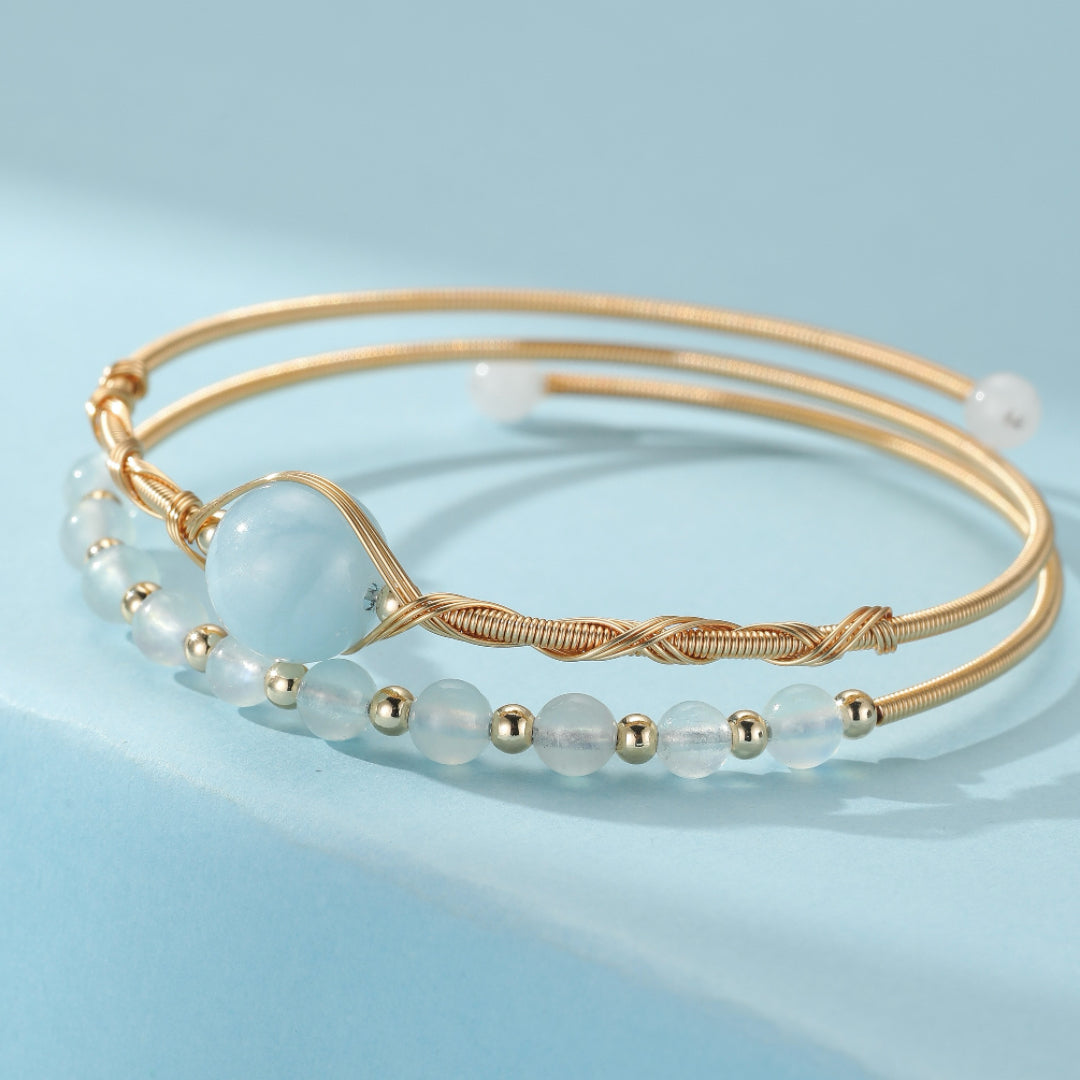 Bracelet de perles d'aigue-marine bleu clair et dorées, avec une perle centrale plus grosse et un design torsadé sur le fil.