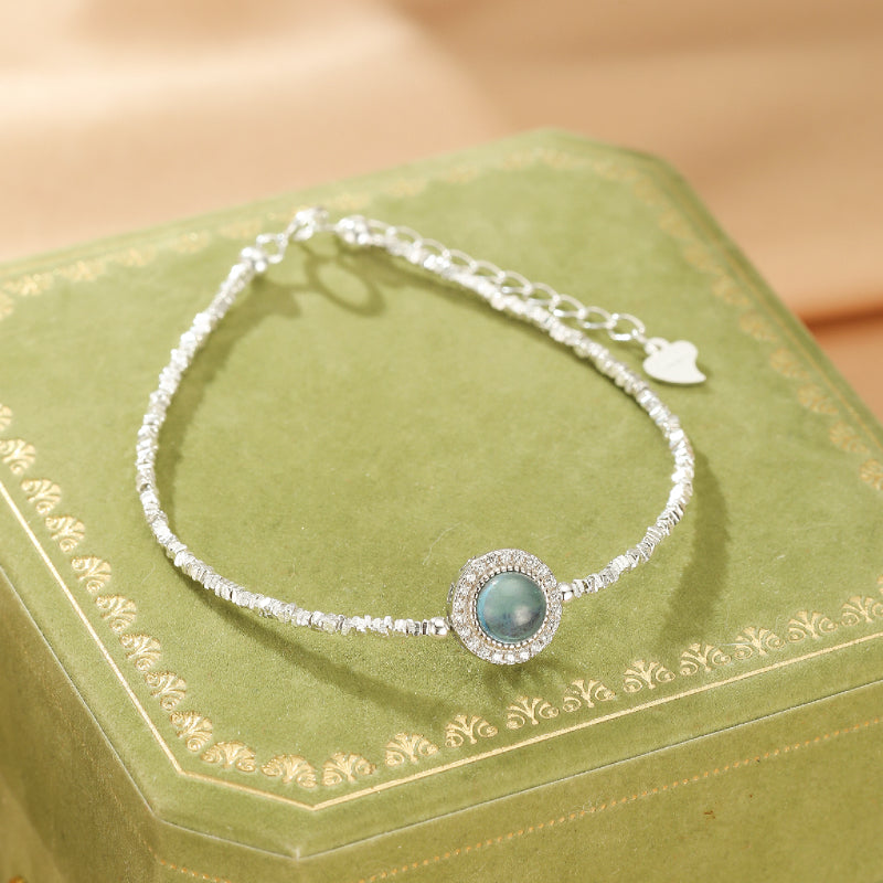 Bracelet en argent avec une pierre d'aigue-marine centrale entourée de petits cristaux scintillants, chaîne fine et réglable.