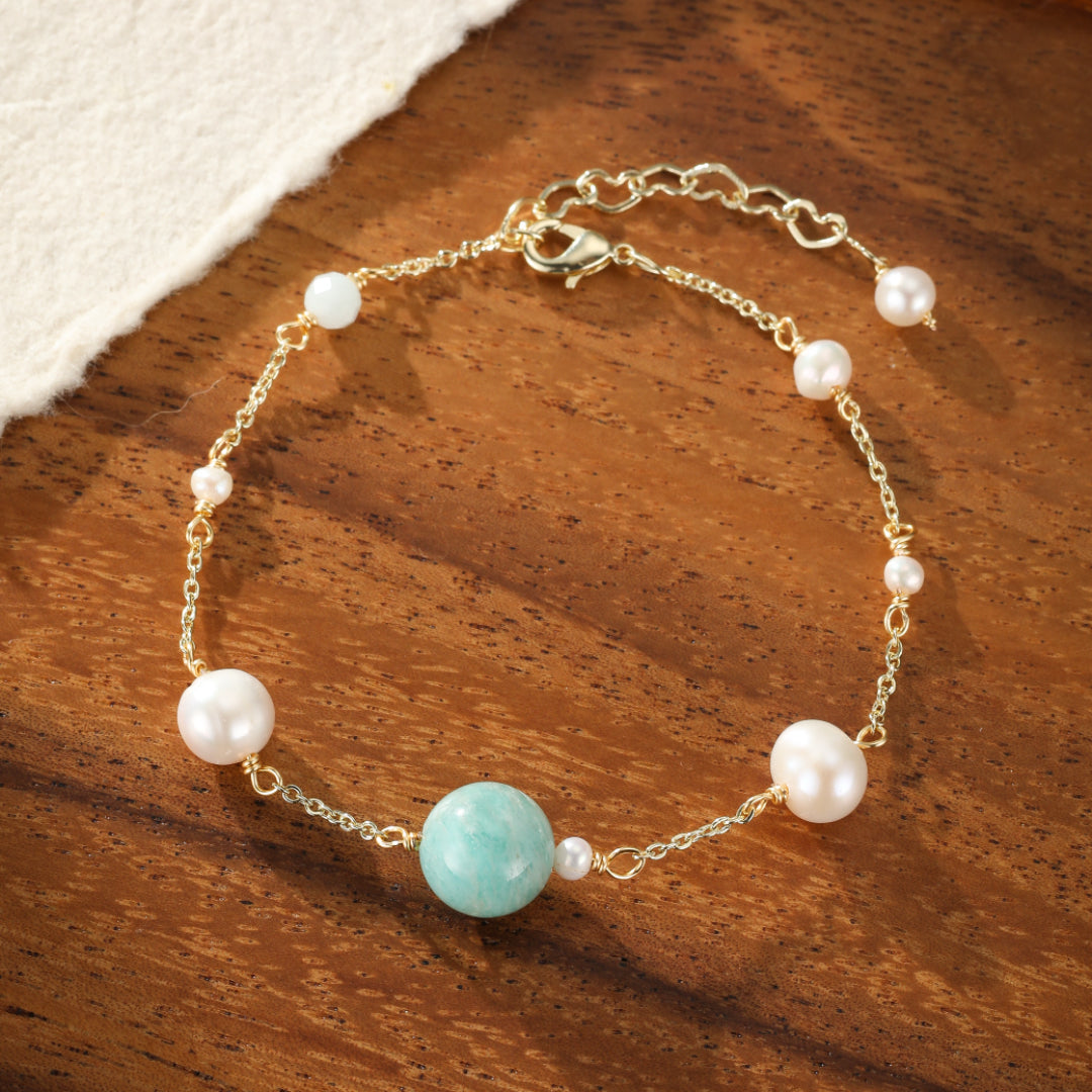 Bracelet délicat avec une perle d'amazonite turquoise centrale, entourée de petites et grosses perles blanches, le tout sur une chaîne dorée et un fermoir mousqueton.