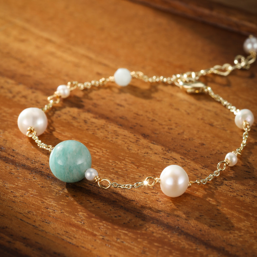 Bracelet Rêve d'Aurore avec une perle d'amazonite centrale, entourée de perles d'eau douce et d'une chaîne dorée délicate, posé sur un fond en bois.