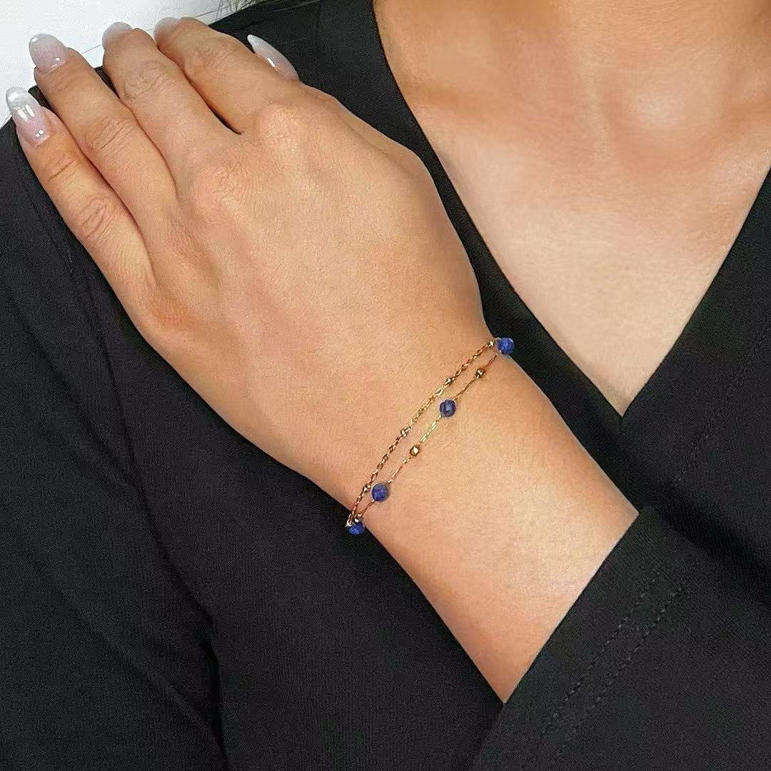 Bracelet fin à double chaîne en or rose avec des perles rondes de lapis-lazuli bleues sur le poignet d'une femme.