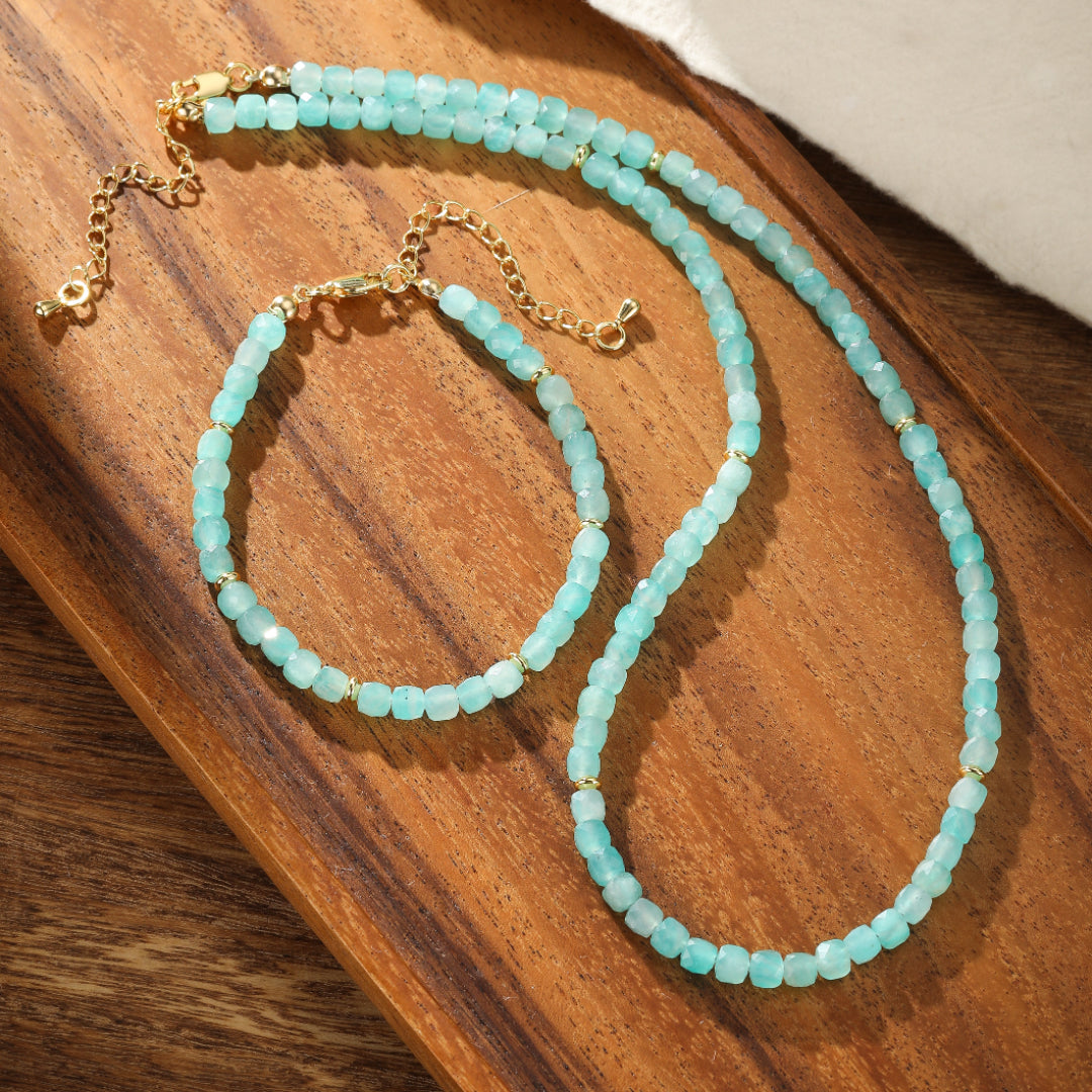 Ensemble de collier et bracelet en amazonite bleue ciel avec des perles dorées, sur un plateau en bois.