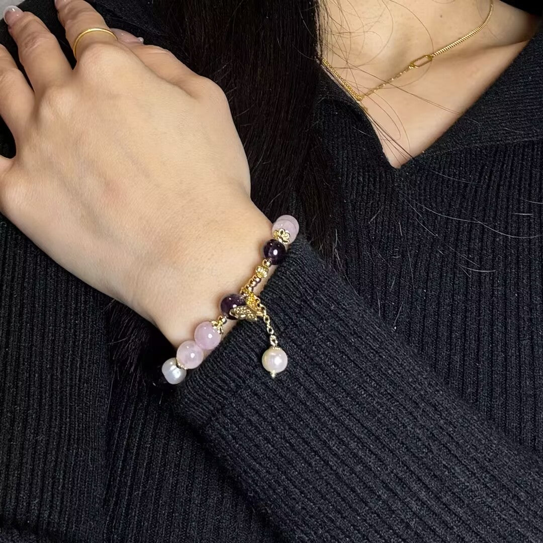 Bracelet élégant en quartz rose, améthyste et perle avec breloque papillon en or, porté au poignet d'une femme.