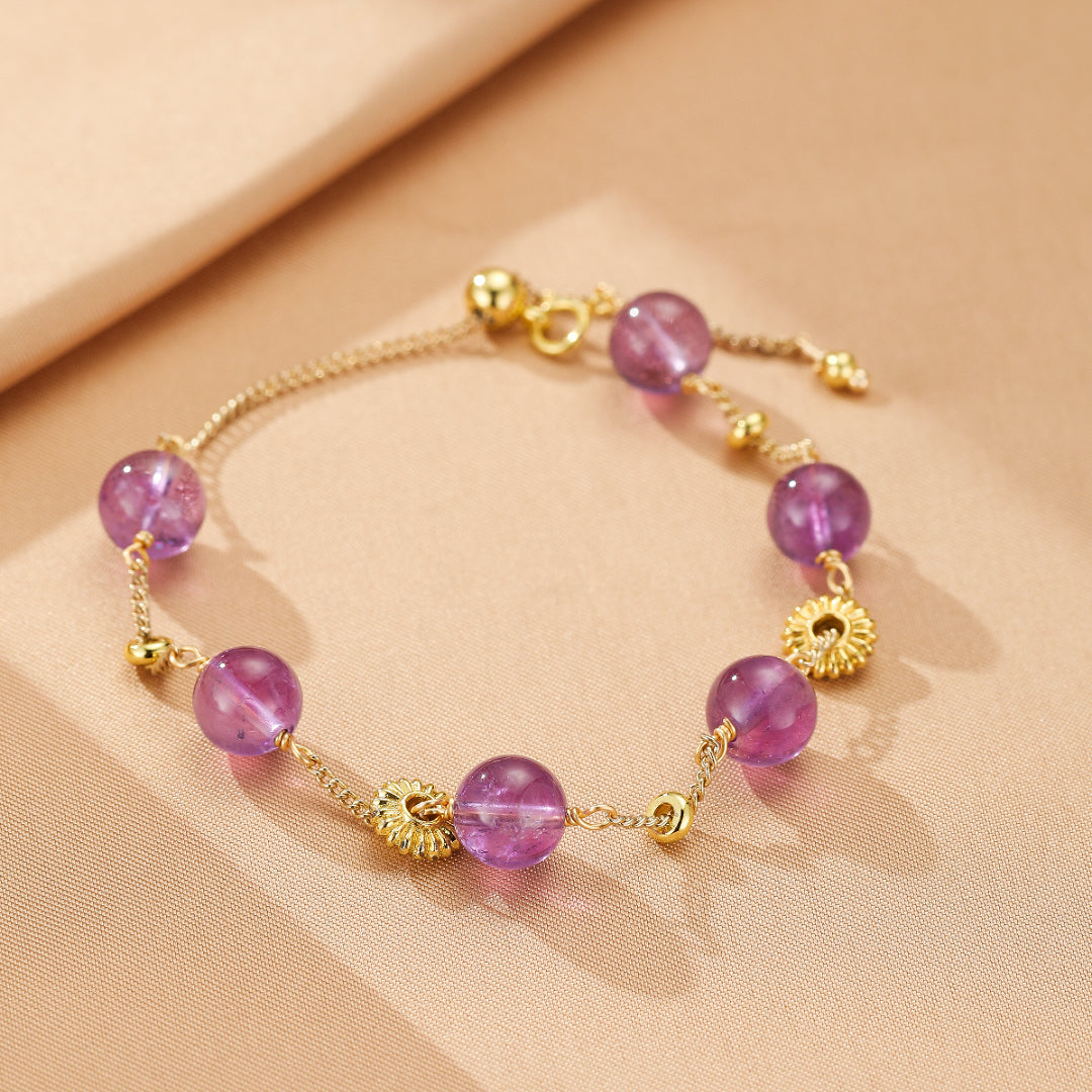 Bracelet ajustable en or avec des perles d'améthyste violettes et des breloques dorées en forme de soleil.