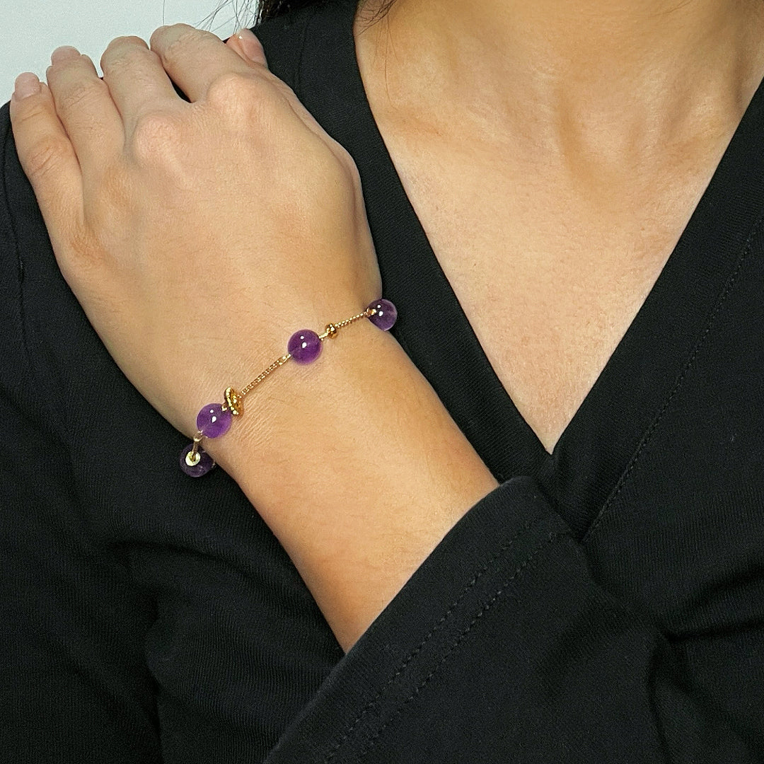 Bracelet en améthyste avec des perles violettes rondes et des petites perles dorées, porté au poignet d'une femme