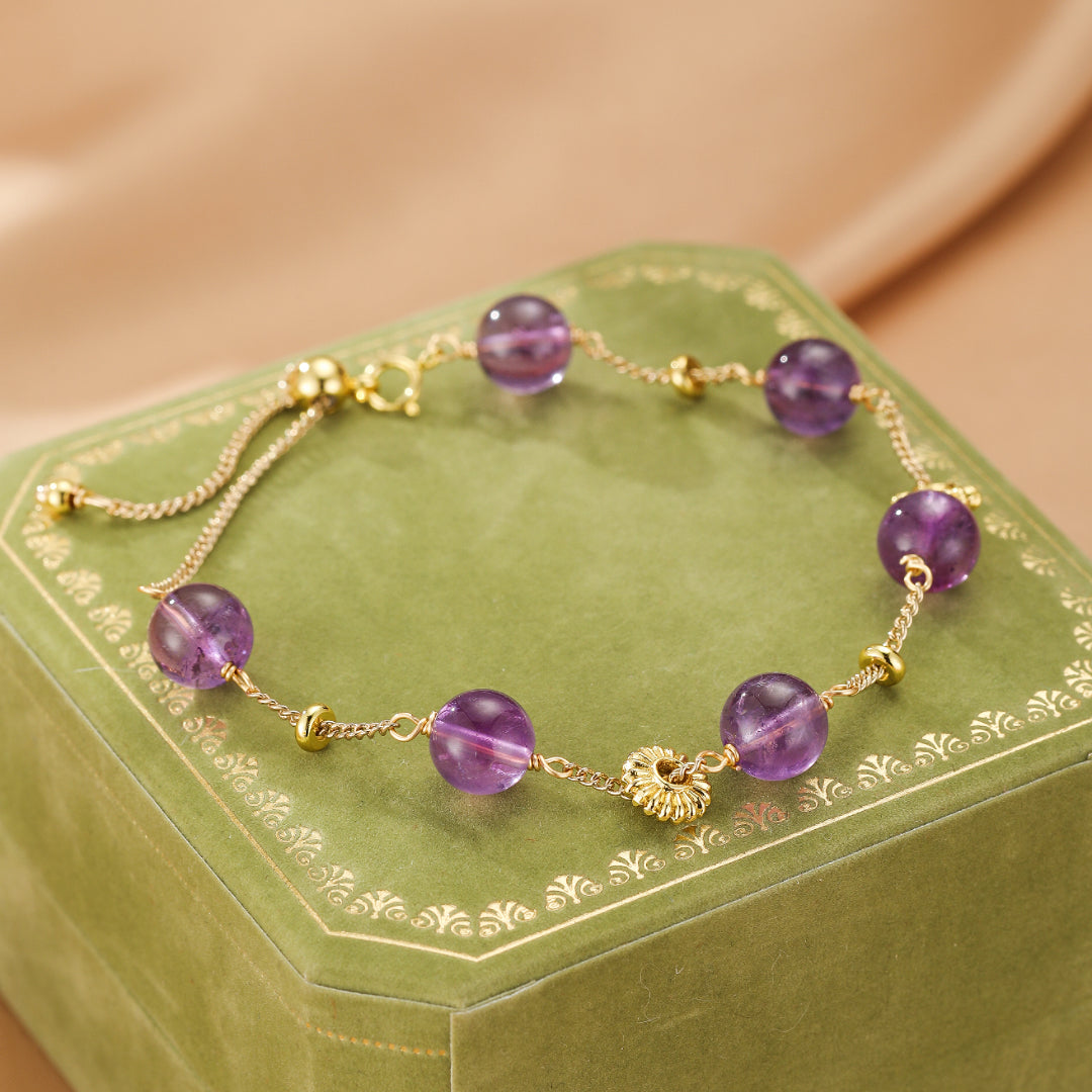 Bracelet ajustable en or avec des perles d'améthyste violettes rondes et des petites perles dorées, présenté sur une boîte verte.