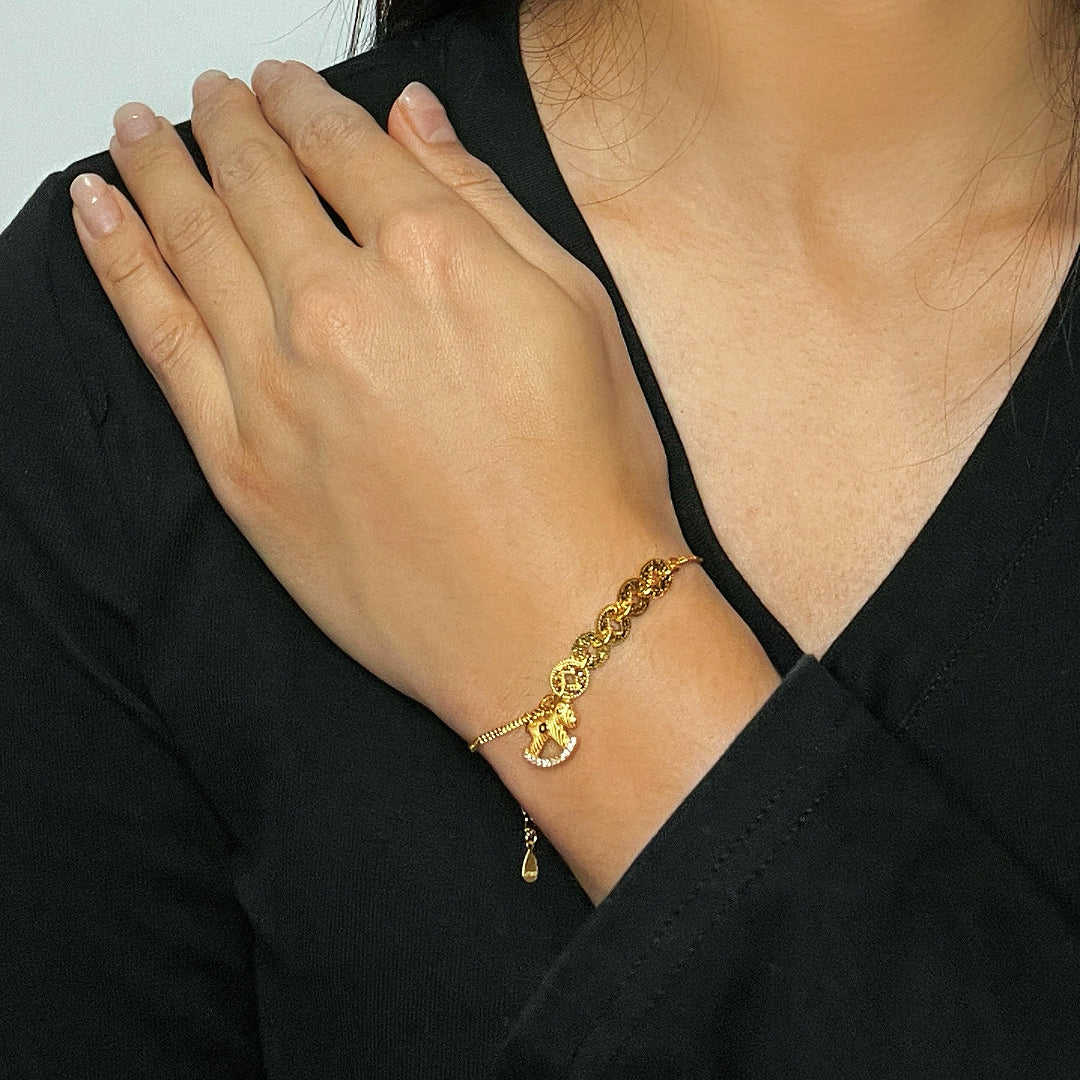 Bracelet en argent plaqué or avec un pendentif cheval incrusté de diamants, porté au poignet d'une femme.