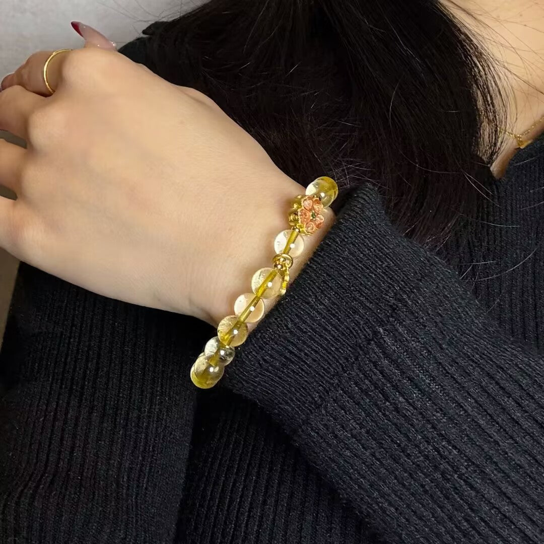 Bracelet en citrine avec une fleur de tiaré et des perles rondes translucides, porté au poignet d'une femme.