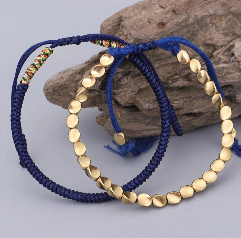 Deux bracelets en cordon bleu foncé ornés de perles dorées, posés sur un morceau de bois.