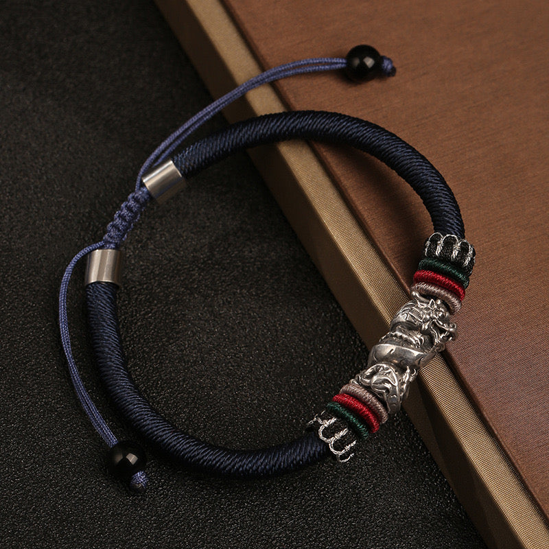Bracelet cordon bleu avec un pendentif en argent représentant un dragon, orné de fils colorés rouges, verts et beiges.